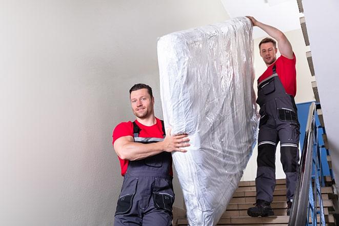 two people carrying a box spring down a staircase in Grundy Center